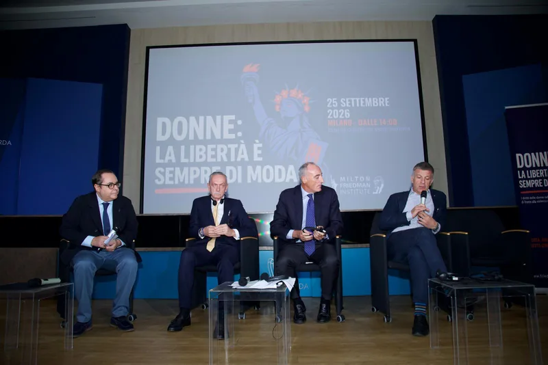 Quattro relatori seduti sul palco davanti allo schermo con il titolo dell’evento
