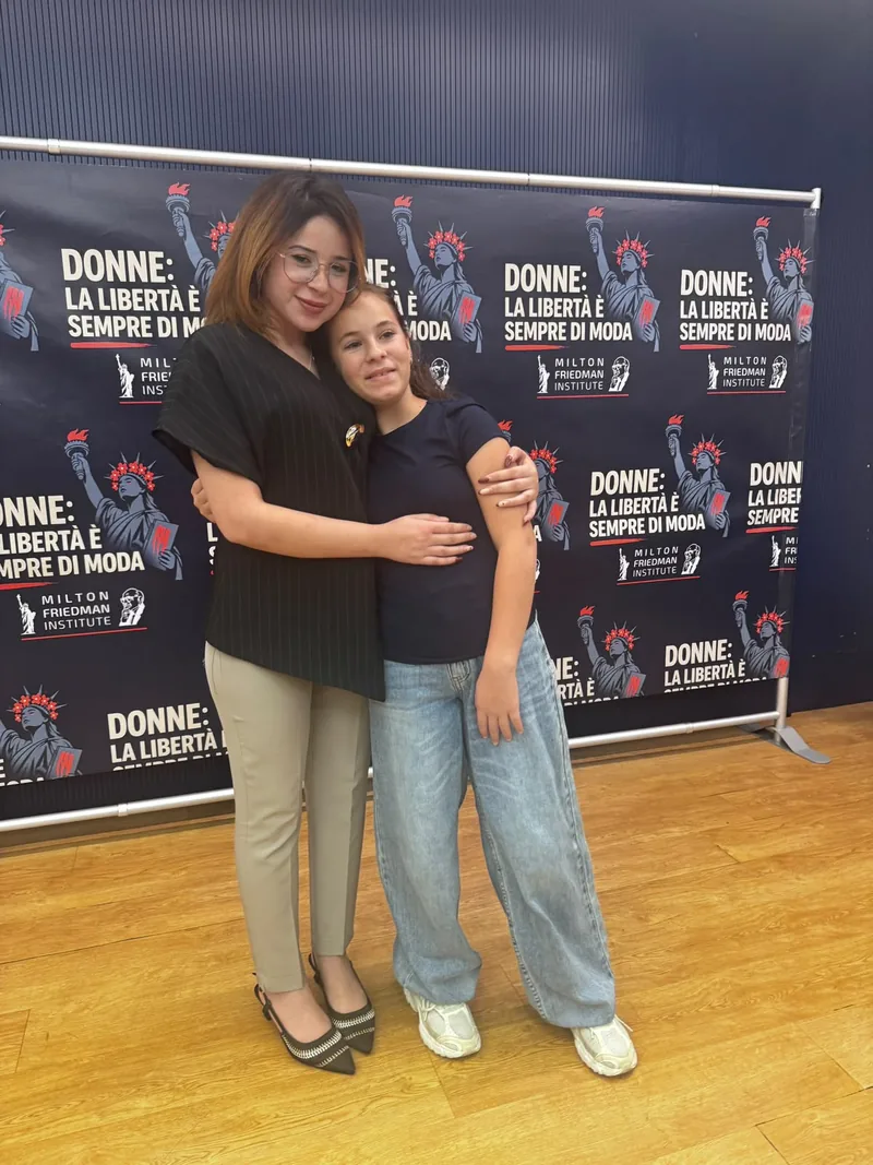 Una giovane donna e una ragazzina abbracciate davanti al backdrop dell’evento