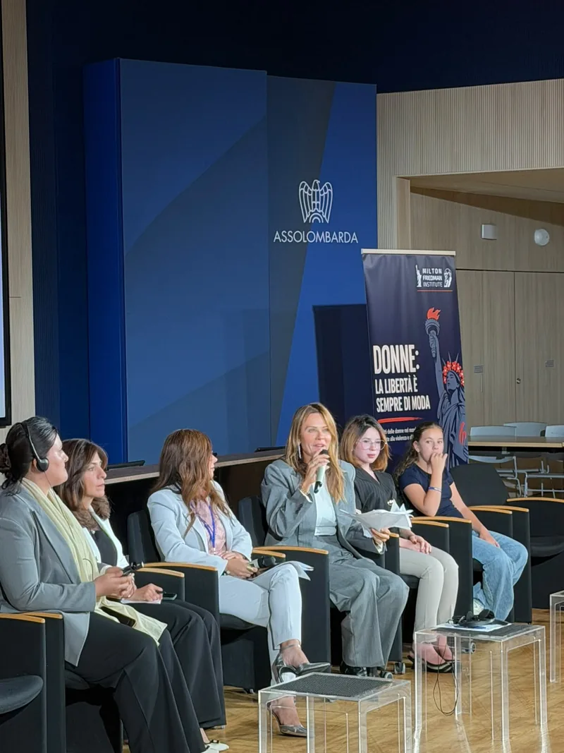 Sei donne sedute sul palco; una parla al microfono