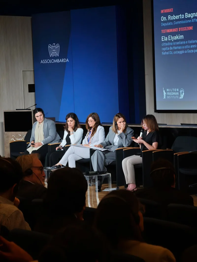 Cinque donne sedute sul palco, una parla al microfono